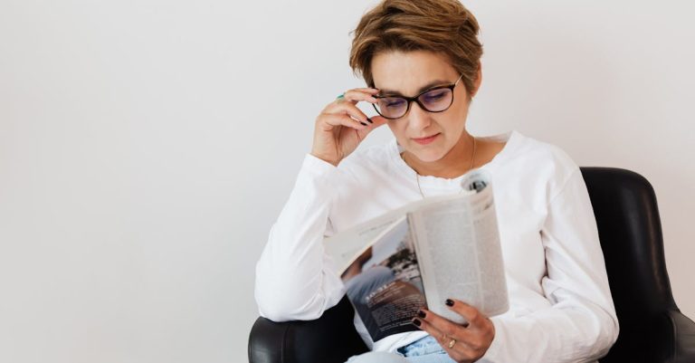 positive-adult-short-haired-female-in-casual-wear-and-eyeglasses-reading-interesting-magazine-while