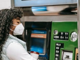 a-woman-wearing-a-face-mask-uses-a-ticket-machine-for-purchasing-fare-in-a-public-setting-reflectin