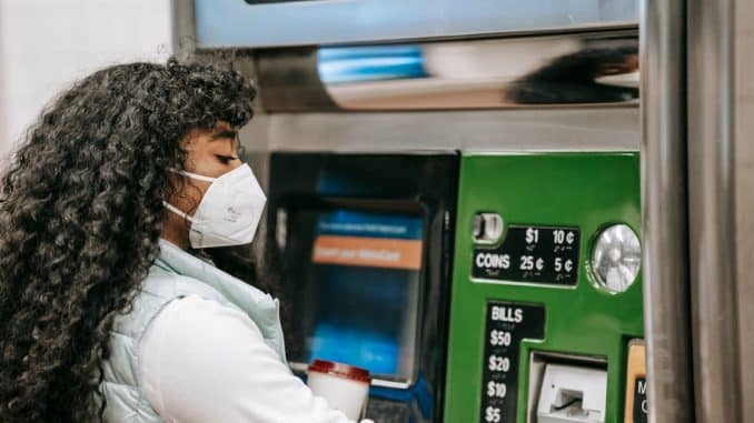 a-woman-wearing-a-face-mask-uses-a-ticket-machine-for-purchasing-fare-in-a-public-setting-reflectin