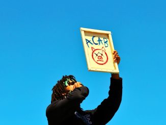 a-protester-raises-a-sign-during-a-demonstration-in-los-angeles-under-a-clear-blue-sky