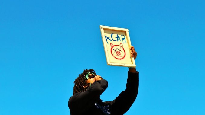 a-protester-raises-a-sign-during-a-demonstration-in-los-angeles-under-a-clear-blue-sky