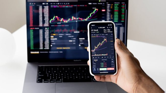 person-checking-stock-market-graphs-on-laptop-and-smartphone-focusing-on-financial-data